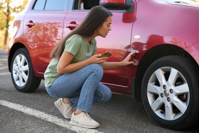 Photo of Stressed woman near car with scratch outdoors