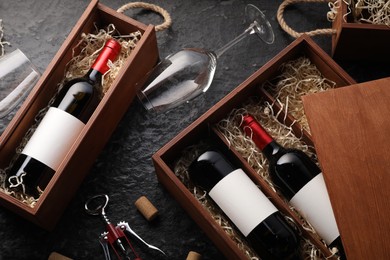 Photo of Bottles of wine in wooden boxes, glasses, corkscrew and corks on dark textured table, above view