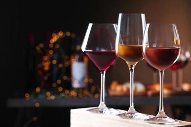 Photo of Glasses with different wines on wooden table against defocused lights. Space for text