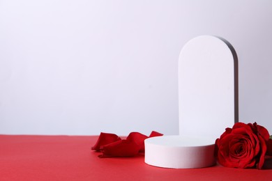 Photo of Stylish presentation for product. Beautiful rose, petals and geometric figures on red table against white background, space for text