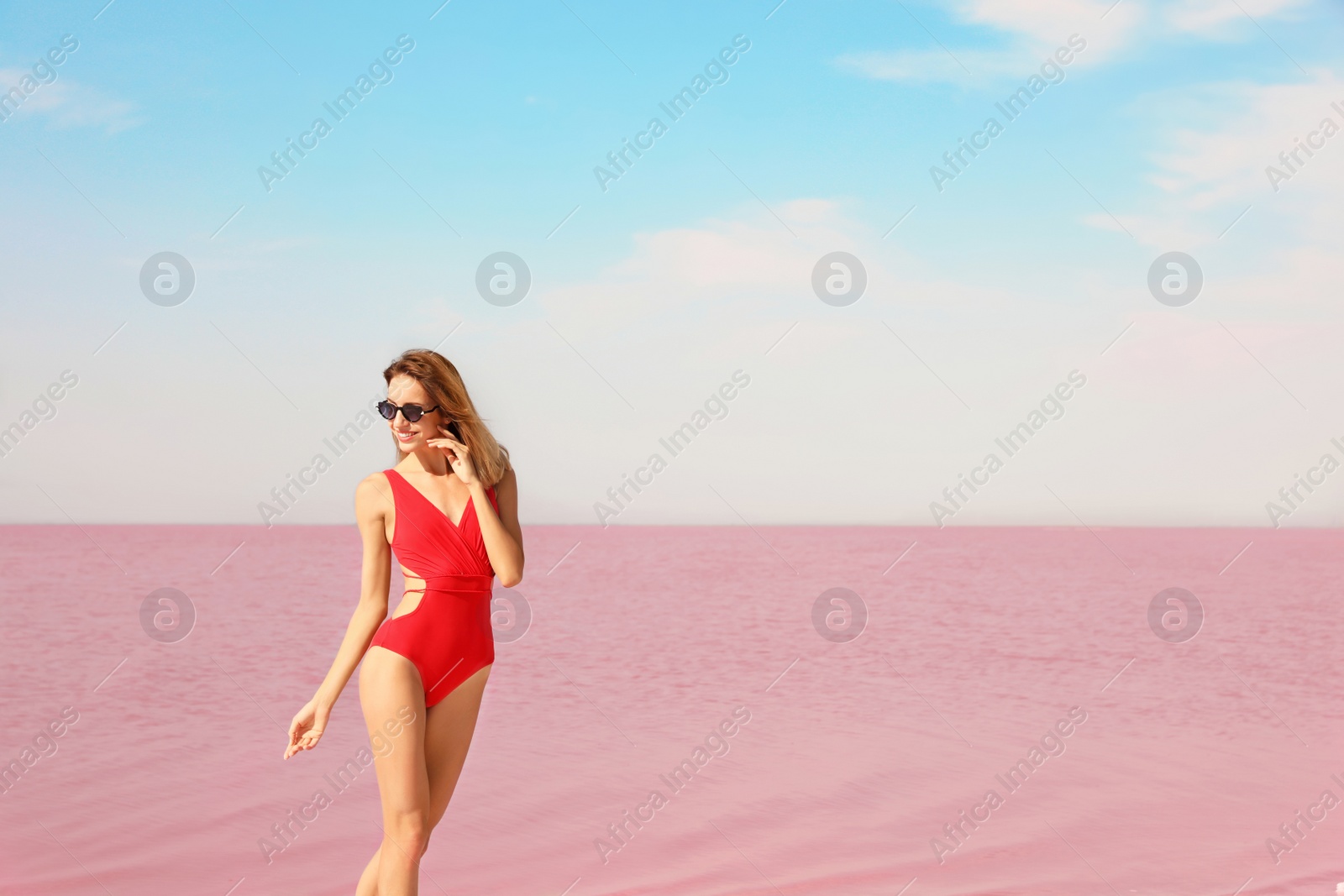 Photo of Beautiful woman in swimsuit posing near pink lake on sunny day