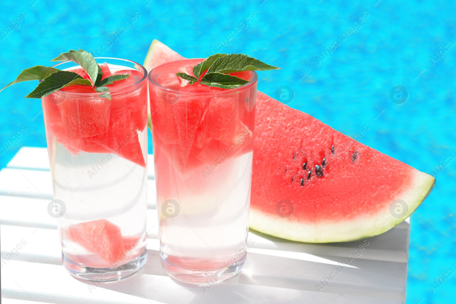 Photo of Refreshing drink in glasses and sliced watermelon near swimming pool outdoors