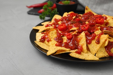 Plate of Mexican nacho chips with sauce on grey table