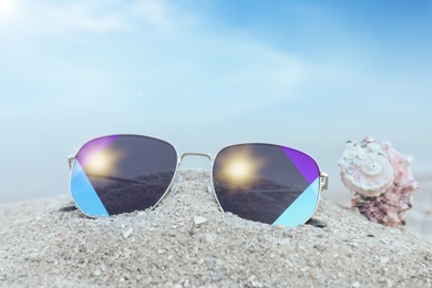 Photo of Stylish sunglasses and shell on sandy beach, closeup
