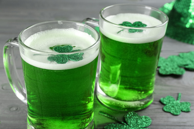 Photo of Green beer and clover leaves on grey wooden table, closeup. St. Patrick's Day celebration