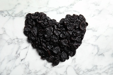 Photo of Heart shaped pile of sweet dried plums on marble background, top view. Healthy fruit