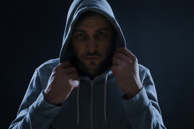 Mysterious man in hoodie on dark background. Dangerous criminal