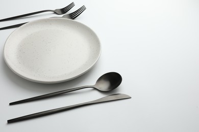 Empty plate, forks, spoon and knife on white background, space for text