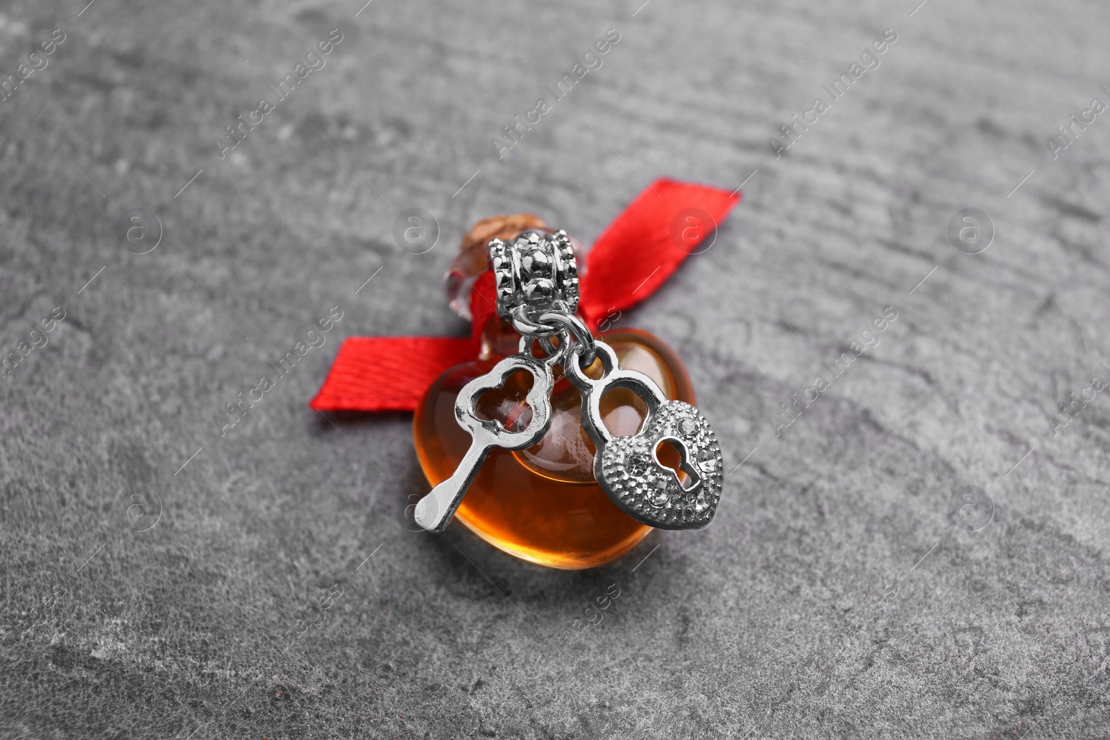 Photo of Heart shaped bottle of love potion with small key and padlock on grey table