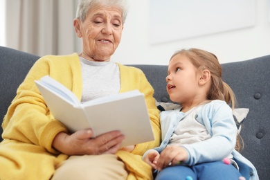 Cute girl and her grandmother reading book at home