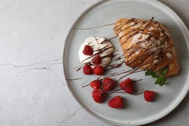 Photo of Delicious croissant with raspberries, cream and chocolate on grey table, top view. Space for text