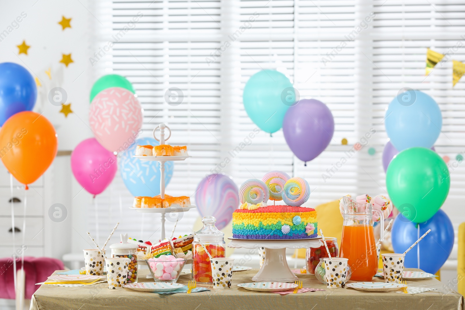 Photo of Bright birthday cake and other treats on table in decorated room