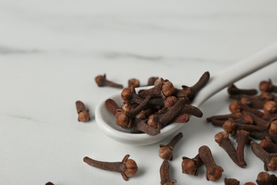 Photo of Aromatic dry cloves and ceramic spoon on white marble table, closeup