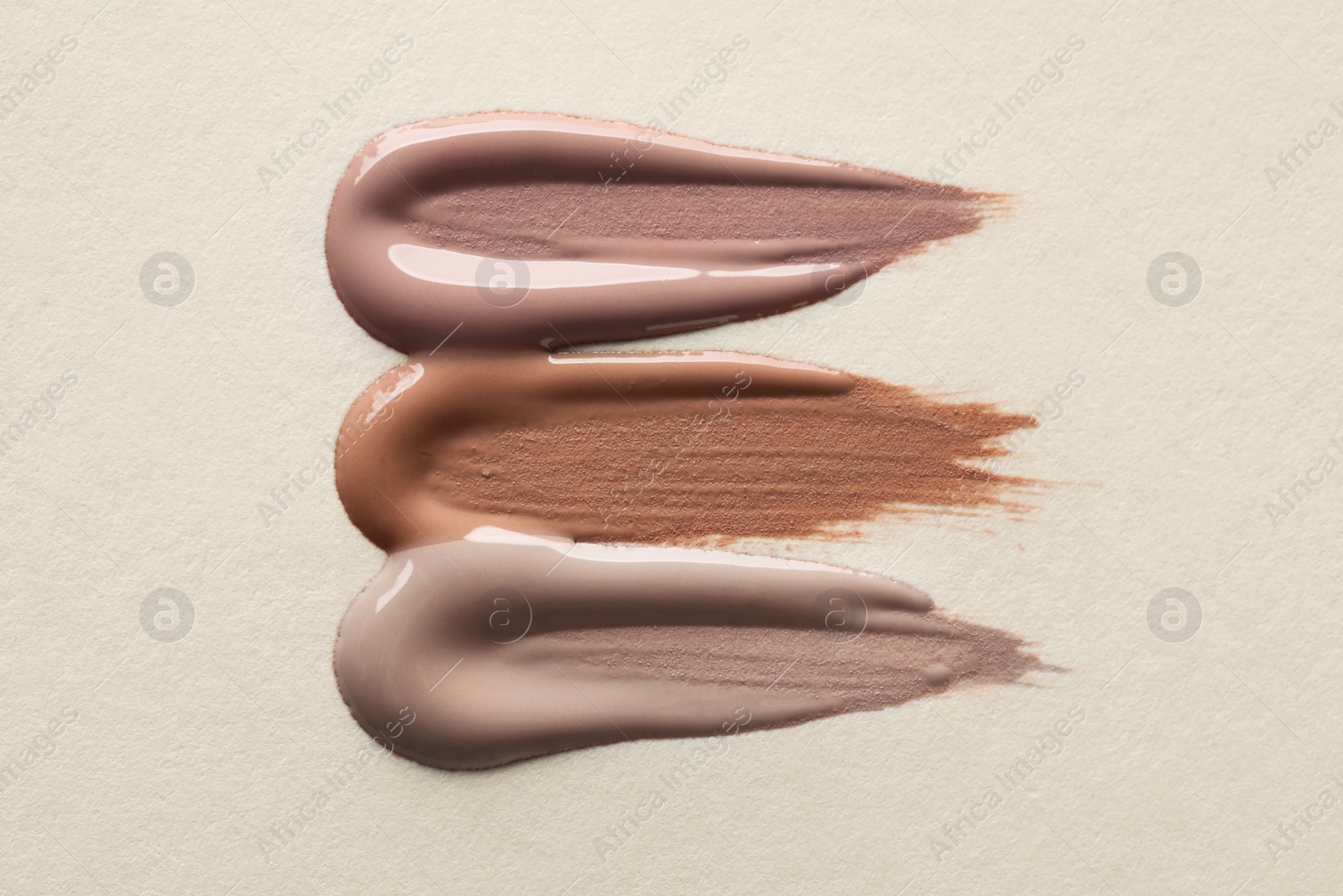 Image of Different shades of liquid foundation on beige background, top view