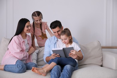 Father reading book to family on sofa in living room