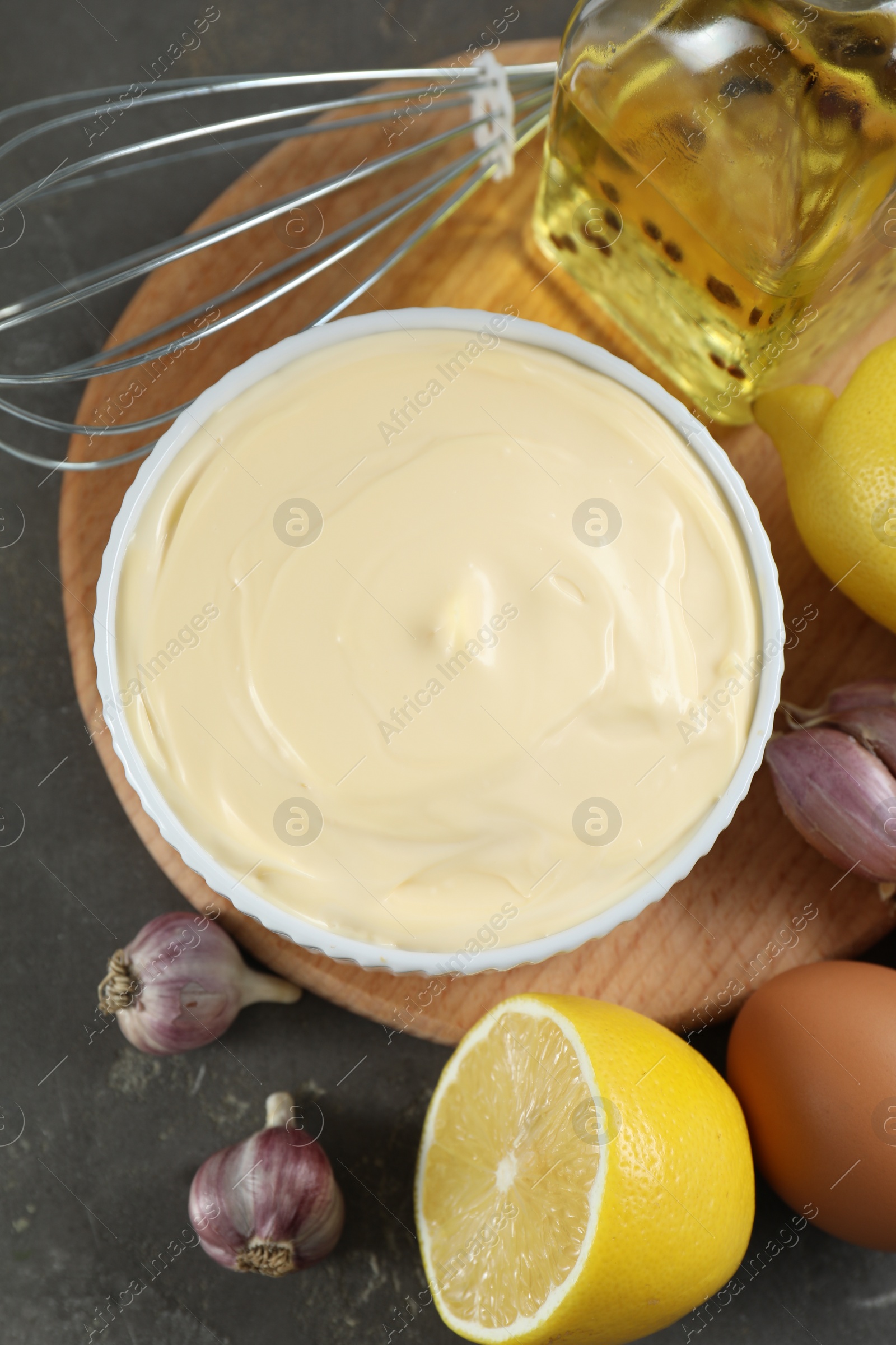 Photo of Fresh mayonnaise sauce in bowl and ingredients on grey table, flat lay