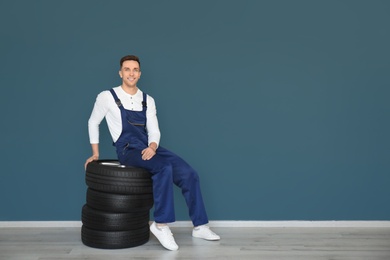 Male mechanic with car tires on grey wall background