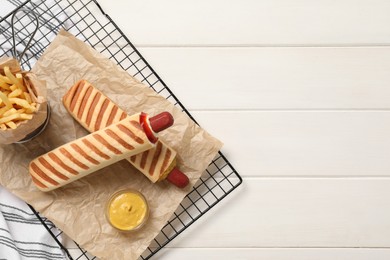 Photo of Delicious french hot dogs, fries and dip sauce on white wooden table, top view. Space for text