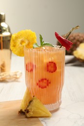Glass of spicy pineapple cocktail with chili pepper on white table