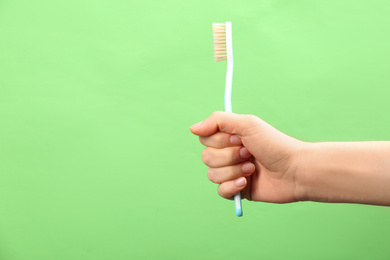 Photo of Woman holding toothbrush with natural bristles on green background, closeup. Space for text