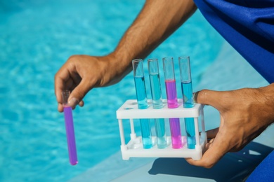 Photo of Man holding test tubes with reagents near swimming pool, closeup