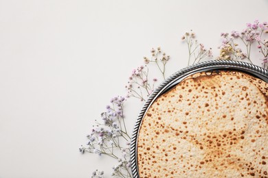 Photo of Tasty matzos and fresh gypsophila flowers on light grey background, flat lay with space for text. Passover (Pesach) celebration