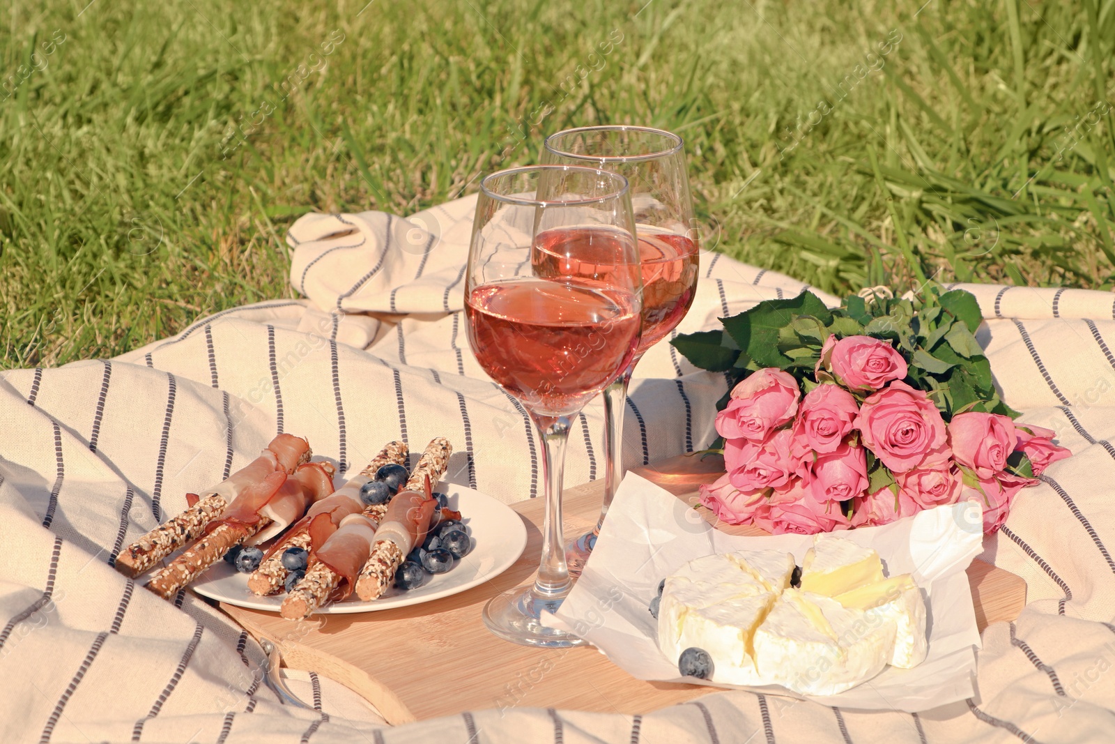 Photo of Glasses of delicious rose wine, flowers and food on picnic blanket outdoors