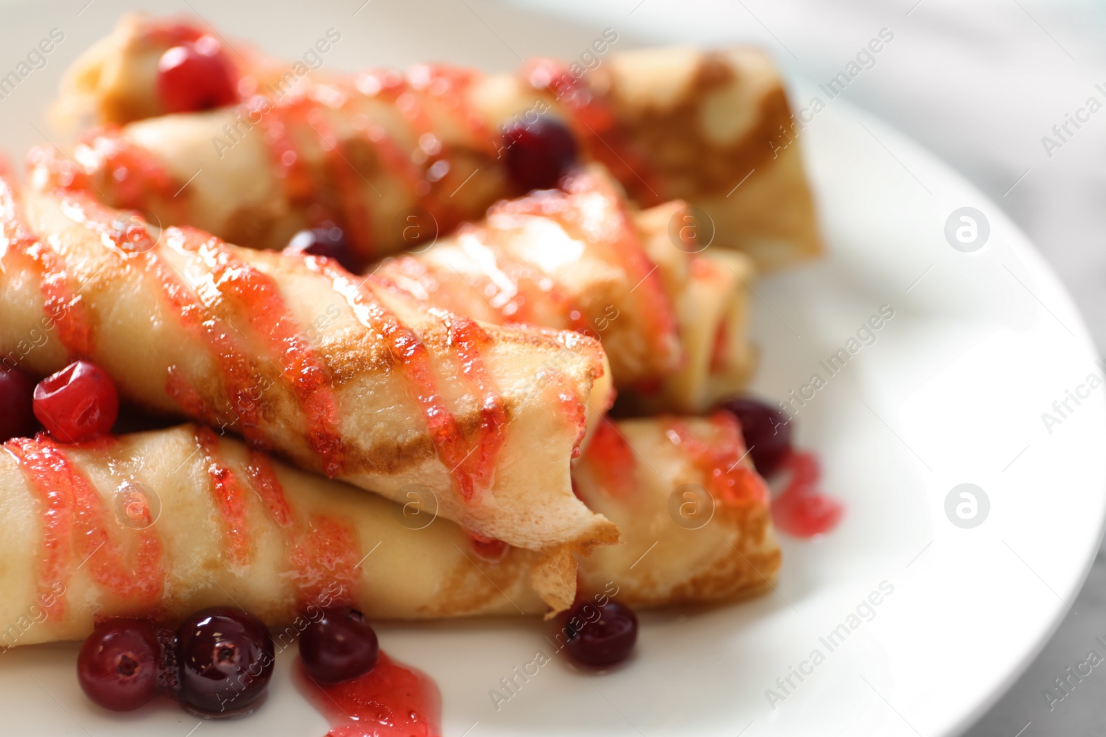 Photo of Thin pancakes with berries and syrup on plate, closeup