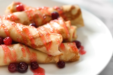 Thin pancakes with berries and syrup on plate, closeup