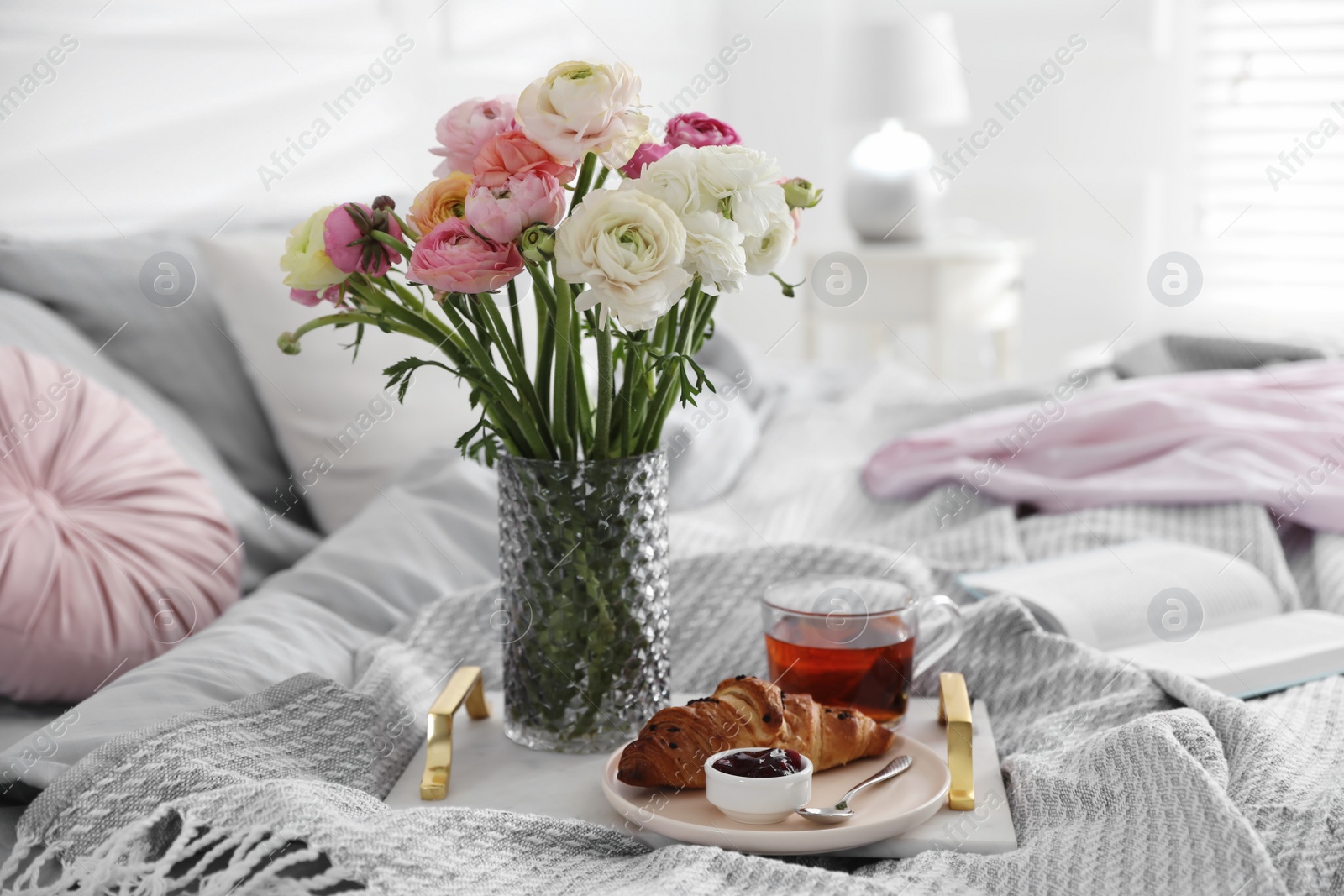 Photo of Bouquet of beautiful ranunculuses, croissant and tea on bed indoors