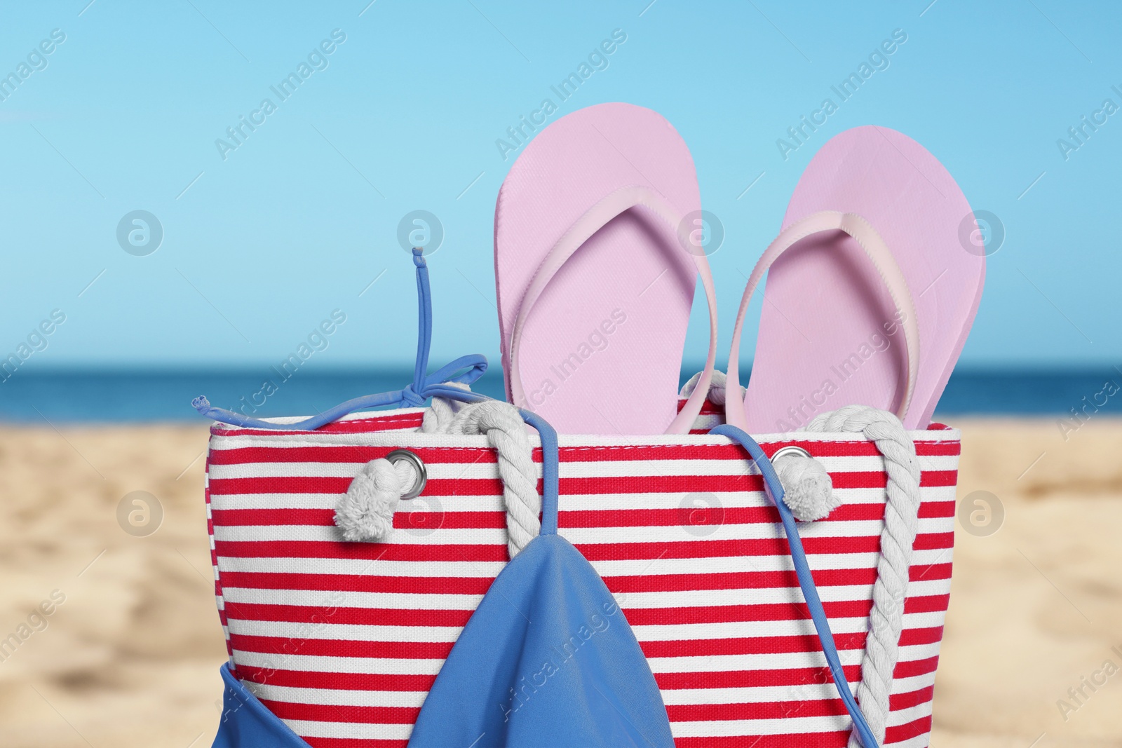 Image of Stylish striped bag and other beach accessories on sand near sea