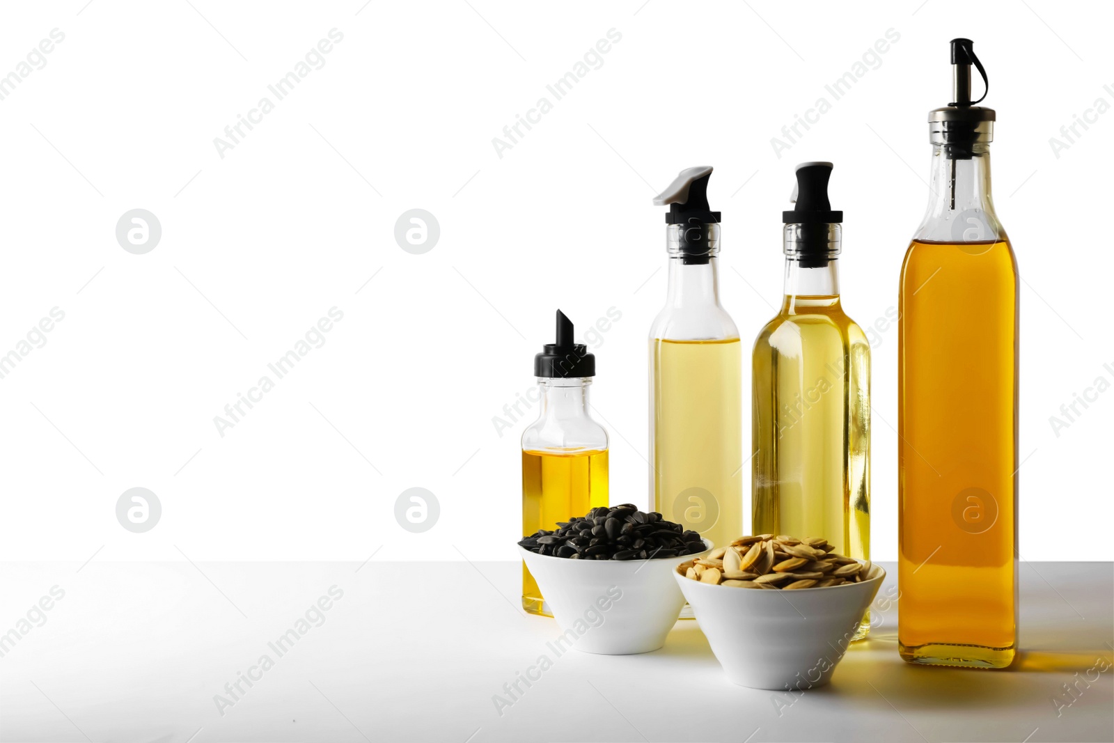 Photo of Bottles of different cooking oils and seeds on white background, space for text