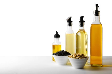 Photo of Bottles of different cooking oils and seeds on white background, space for text