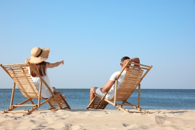 Photo of Young couple relaxing in deck chairs on beach