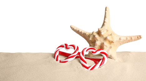 Photo of Beautiful starfish and candy cane party sunglasses on sand against white background. Christmas vacation