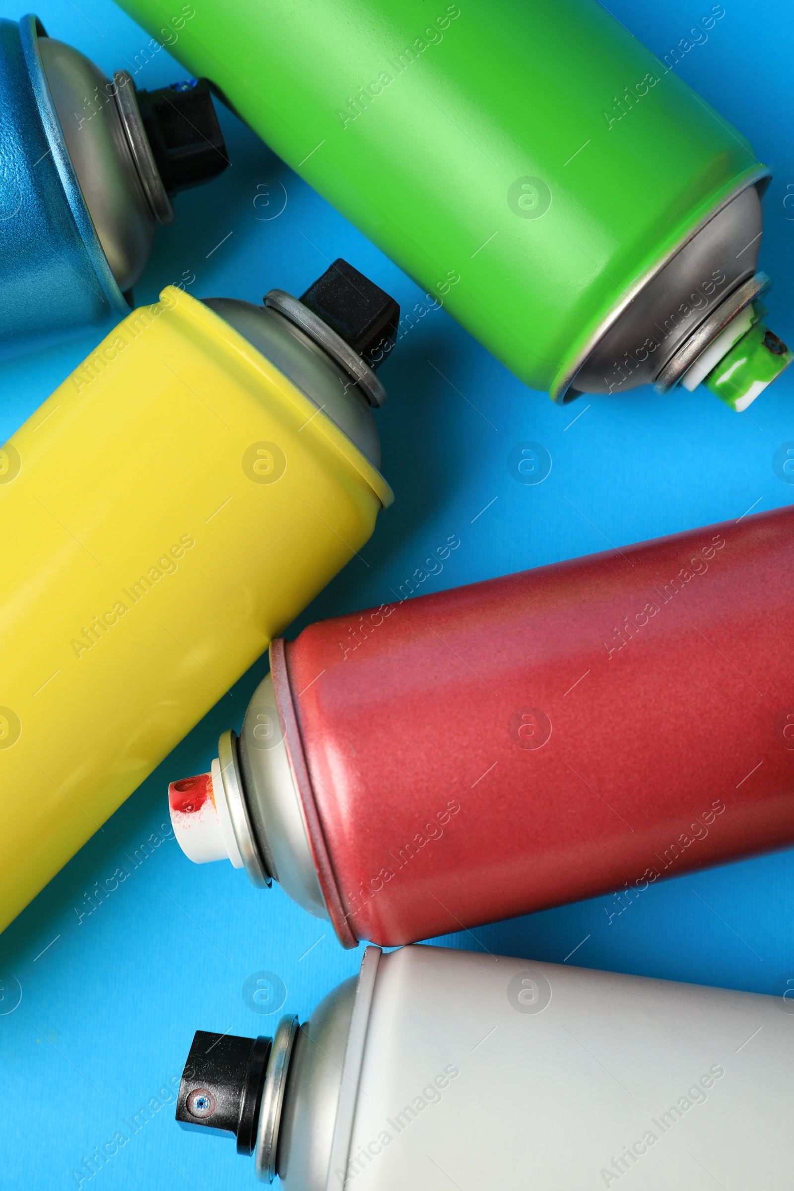 Photo of Cans of different graffiti spray paints on light blue background, flat lay