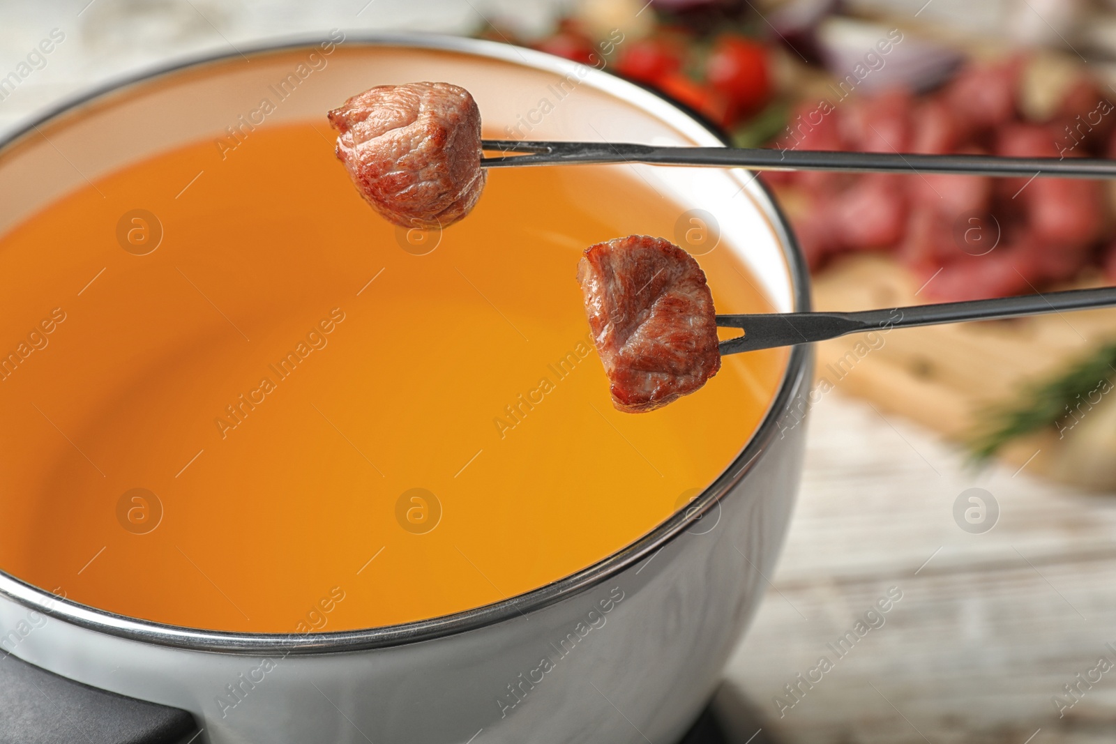 Photo of Dipping meat into fondue pot with oil on table, closeup