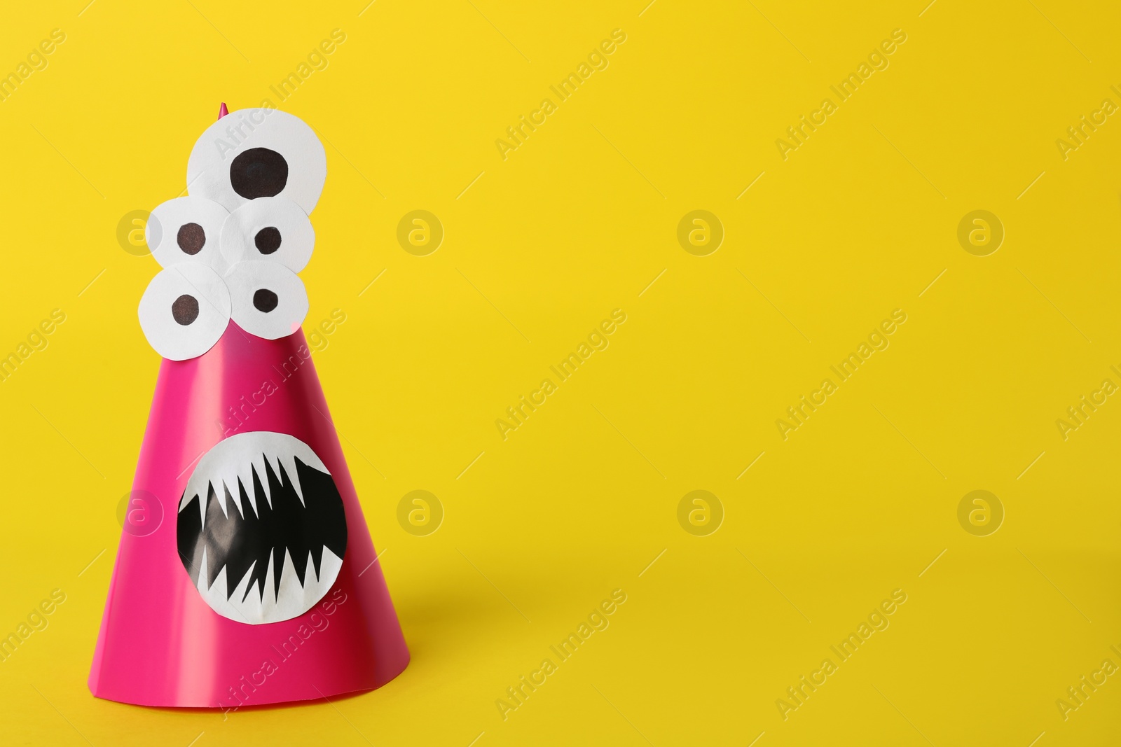 Photo of Funny pink monster on yellow background, space for text. Halloween decoration