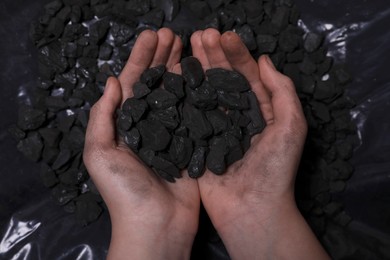 Woman with handful of coal over pile, top view