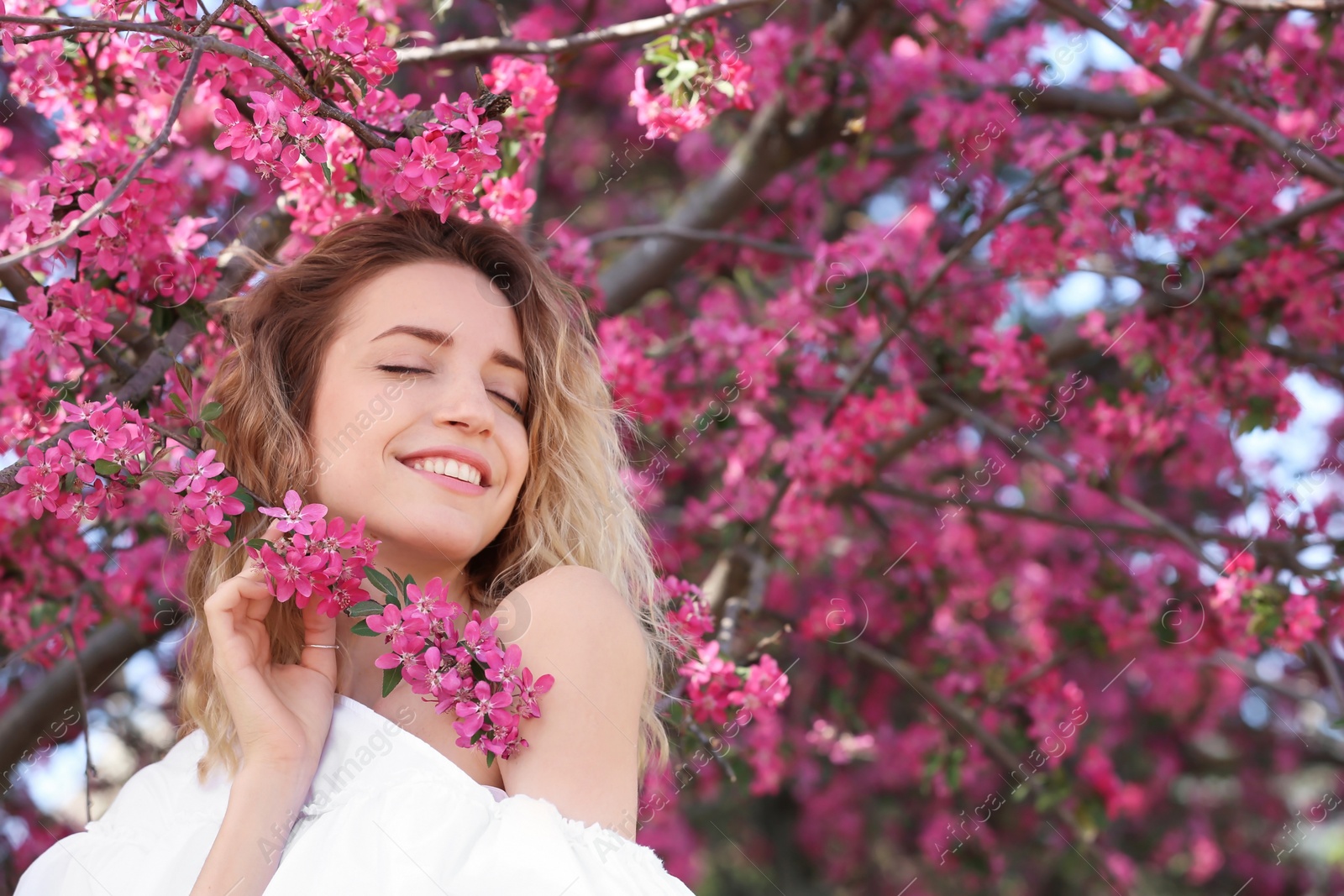 Photo of Attractive young woman posing near blossoming tree on sunny spring day