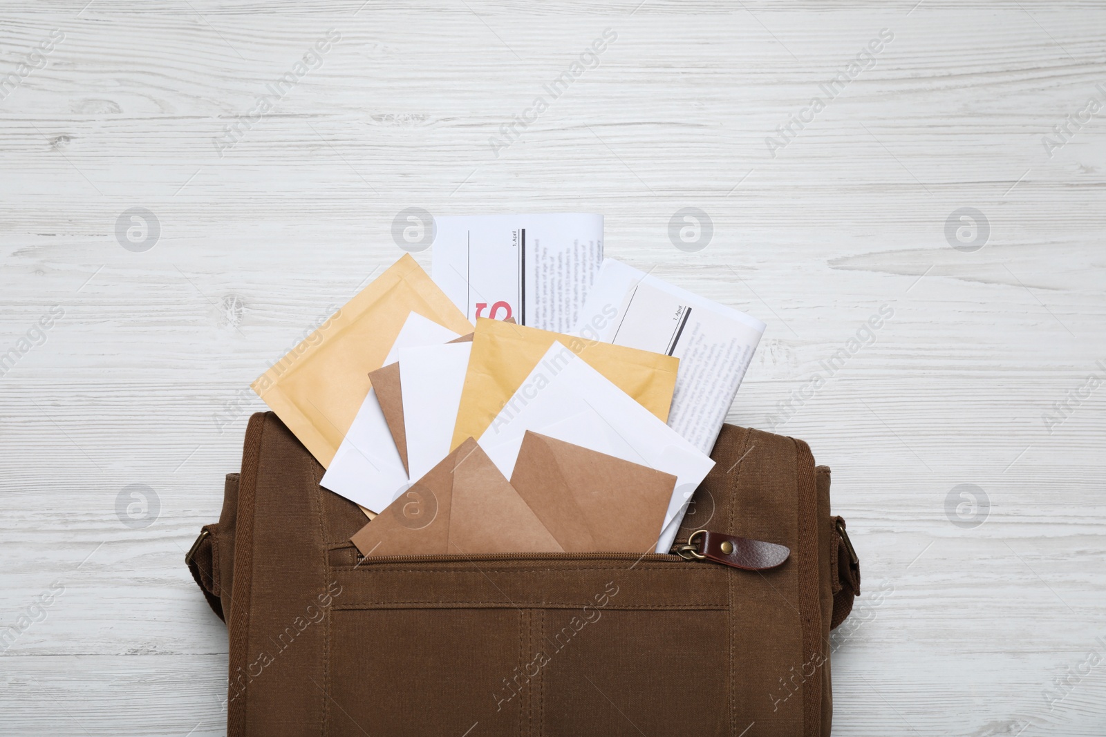 Photo of Brown postman bag with newspapers and mails on white wooden table, flat lay
