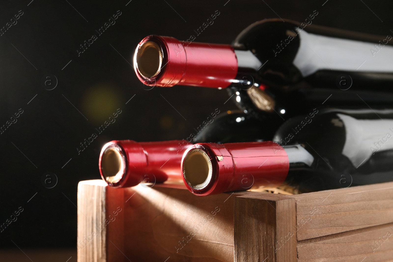 Photo of Wooden crate with bottles of wine on dark background, closeup