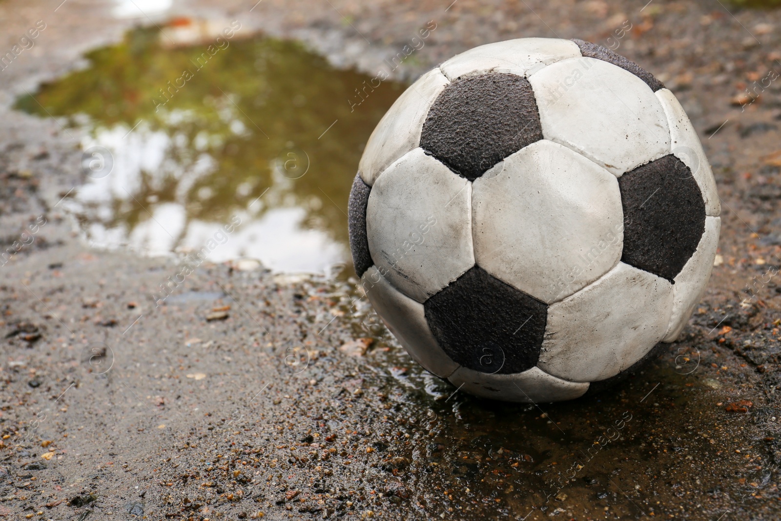 Photo of Dirty soccer ball in muddy puddle, space for text