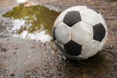 Photo of Dirty soccer ball in muddy puddle, space for text
