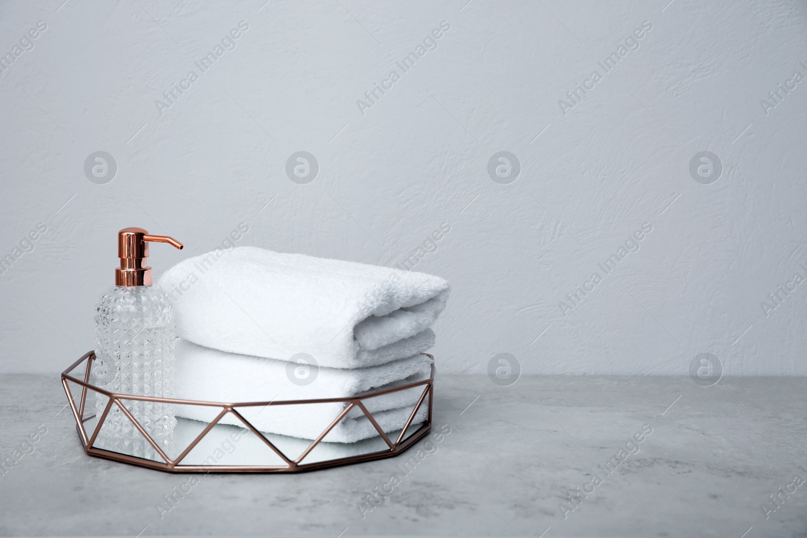 Photo of Tray with towels and soap dispenser on table against grey background