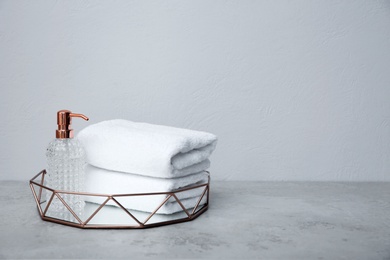 Photo of Tray with towels and soap dispenser on table against grey background