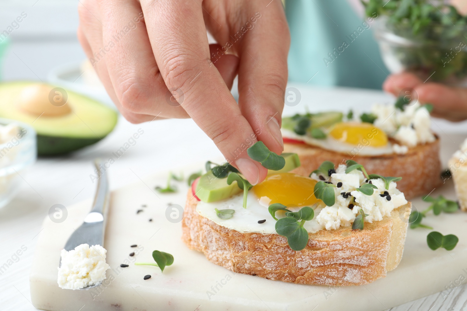 Photo of Woman putting microgreen onto sandwich at table, closeup