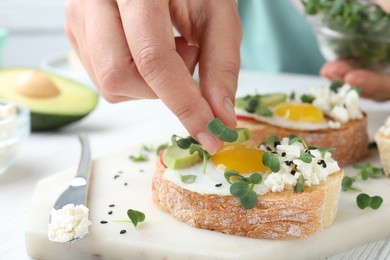 Woman putting microgreen onto sandwich at table, closeup