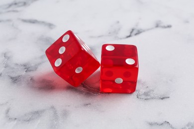 Two red game dices on white marble table, closeup