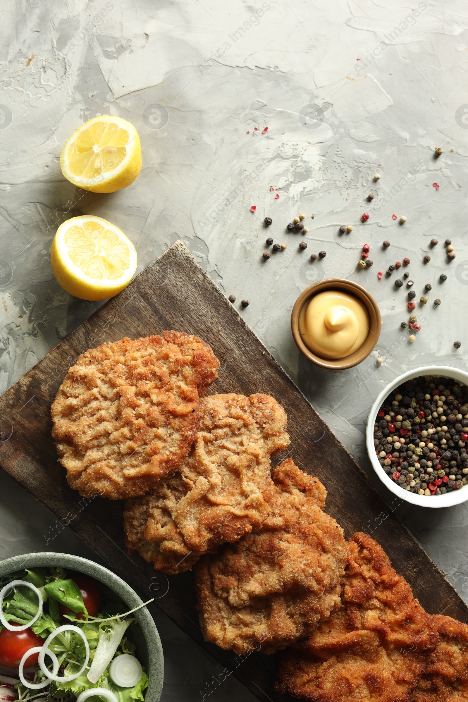 Photo of Tasty schnitzels served with lemon, salad and sauce on grey table, flat lay